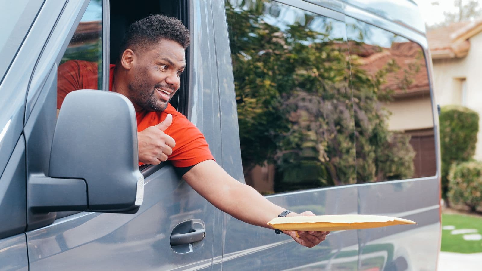 Stallionex courier smiling and handing a parcel out of a delivery van window